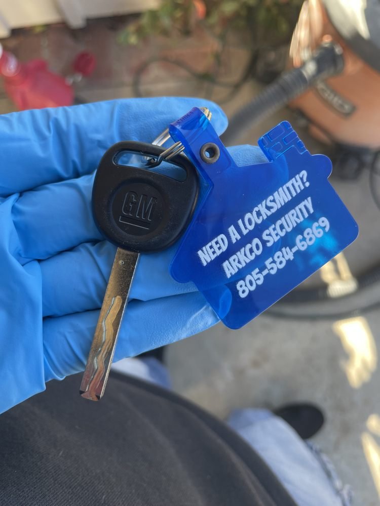 A new car key on an Arkco Security tag, held in a gloved hand