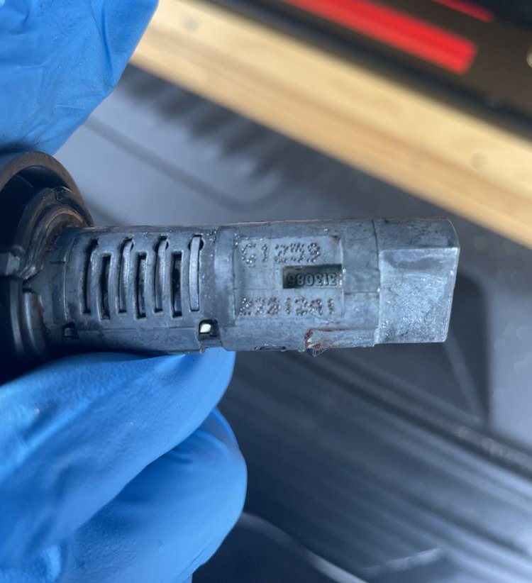 A worn ignition lock cylinder pulled out of a car, held in a gloved hand